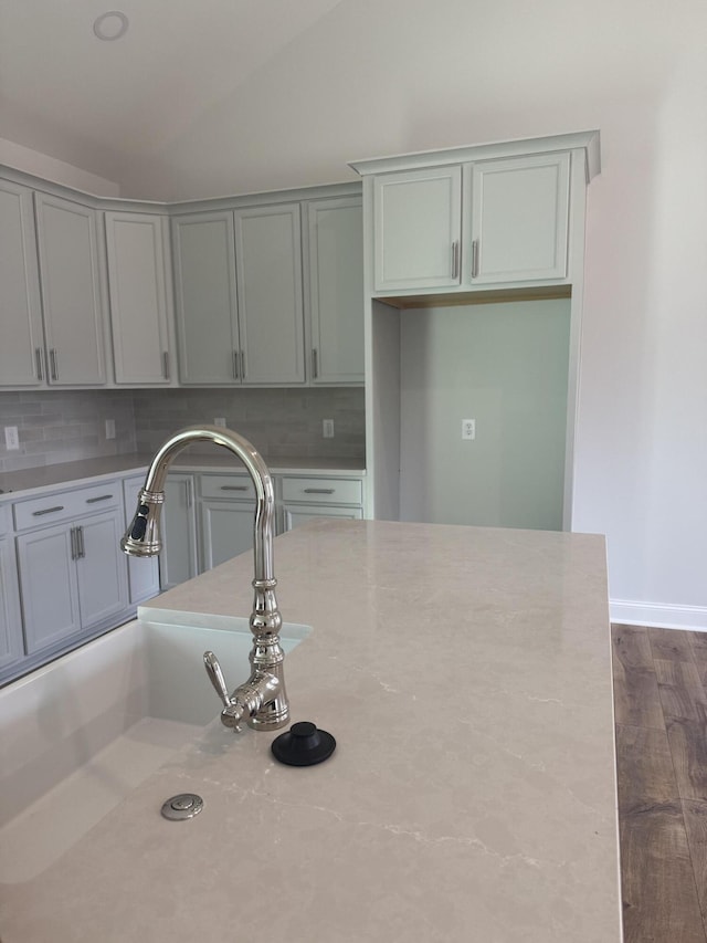 kitchen featuring light stone countertops, dark hardwood / wood-style flooring, tasteful backsplash, sink, and gray cabinets