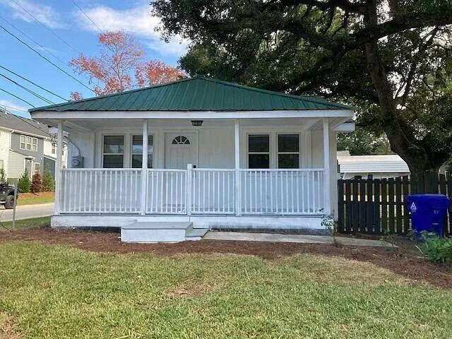 bungalow-style house featuring covered porch, metal roof, fence, and a front lawn