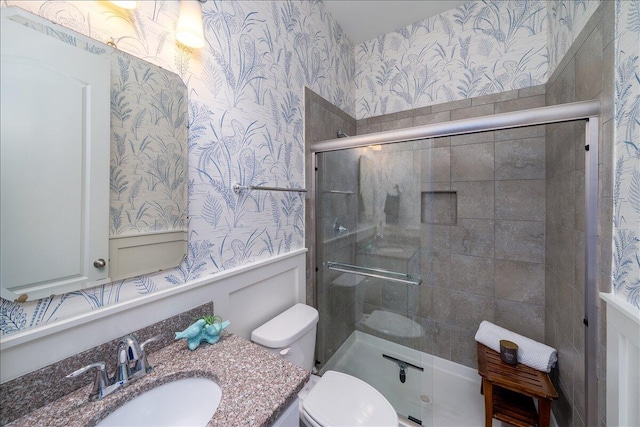 bathroom with a shower with door, toilet, vanity, and wallpapered walls