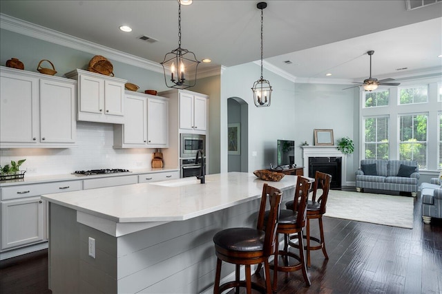 kitchen with ornamental molding, decorative backsplash, ceiling fan with notable chandelier, arched walkways, and stainless steel appliances