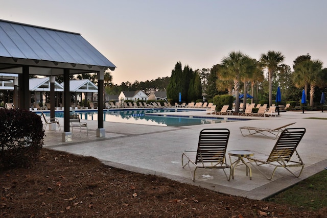 pool at dusk featuring a community pool and a patio