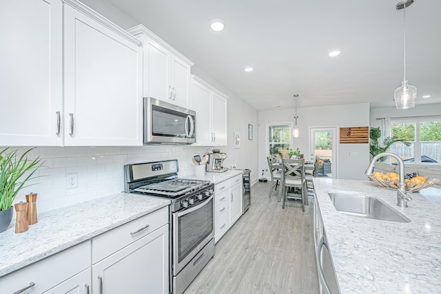 kitchen featuring stainless steel appliances, white cabinetry, hanging light fixtures, and sink