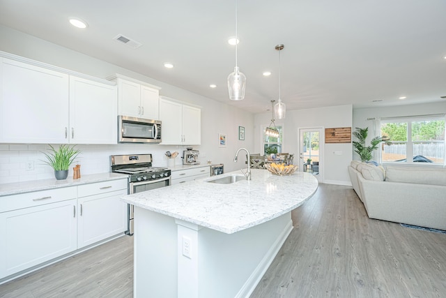 kitchen featuring appliances with stainless steel finishes, sink, a center island with sink, white cabinetry, and hanging light fixtures