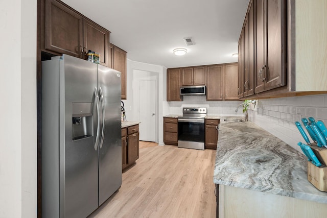 kitchen featuring light stone countertops, backsplash, stainless steel appliances, sink, and light hardwood / wood-style flooring