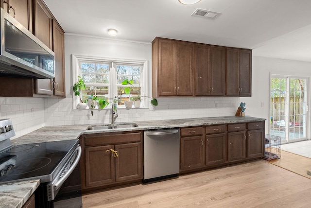 kitchen featuring backsplash, sink, light stone countertops, light hardwood / wood-style floors, and stainless steel appliances