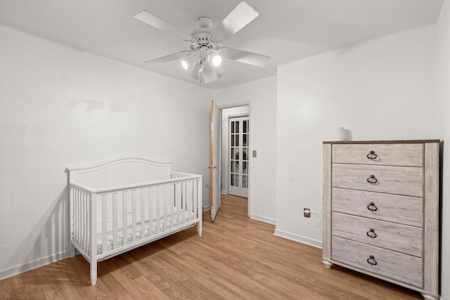 bedroom with light wood-type flooring, a nursery area, and ceiling fan