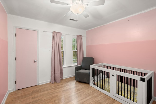 bedroom with ceiling fan, a nursery area, and light wood-type flooring