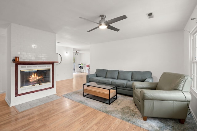 living room featuring a large fireplace, light hardwood / wood-style flooring, and ceiling fan