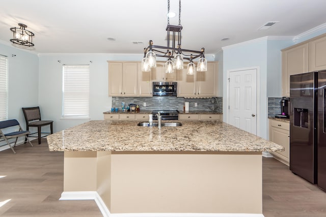 kitchen with black fridge with ice dispenser, light hardwood / wood-style floors, cream cabinetry, and an island with sink