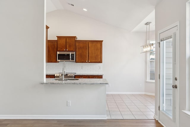 kitchen featuring lofted ceiling, hanging light fixtures, light hardwood / wood-style flooring, decorative backsplash, and light stone counters