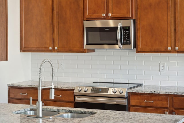 kitchen featuring backsplash, light stone countertops, sink, and appliances with stainless steel finishes