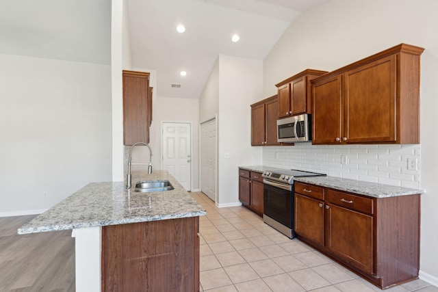 kitchen featuring sink, stainless steel appliances, tasteful backsplash, light stone counters, and light tile patterned floors