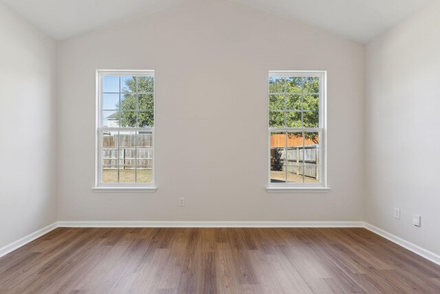 empty room with plenty of natural light, lofted ceiling, and hardwood / wood-style flooring