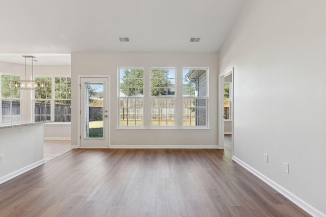 empty room with a chandelier, wood-type flooring, and vaulted ceiling