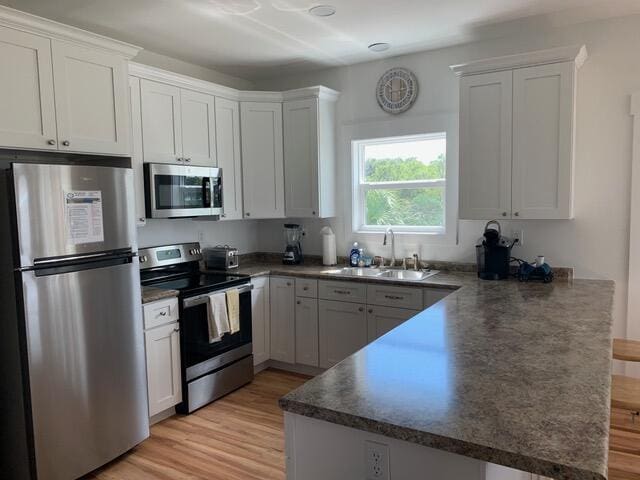 kitchen featuring a peninsula, a sink, appliances with stainless steel finishes, white cabinetry, and dark countertops