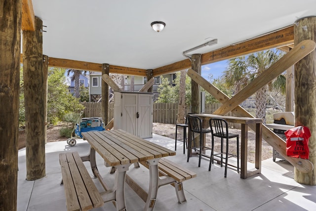 view of patio with outdoor dining space, an outbuilding, a fenced backyard, and a shed