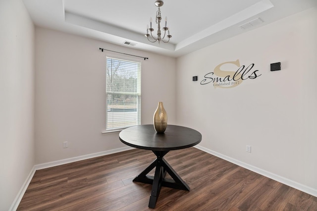 dining space with a tray ceiling, dark hardwood / wood-style flooring, and a notable chandelier