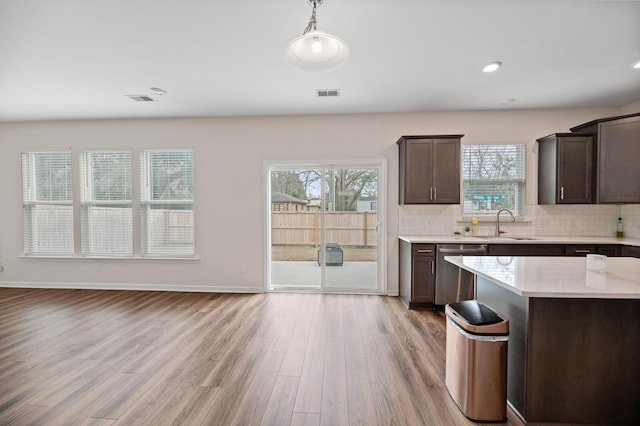 kitchen with plenty of natural light, stainless steel dishwasher, decorative light fixtures, and light hardwood / wood-style flooring