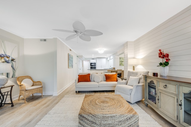 living room with wooden walls, light hardwood / wood-style flooring, and ceiling fan