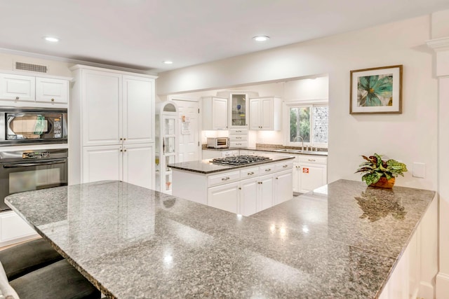 kitchen featuring a kitchen breakfast bar, a spacious island, sink, white cabinets, and black appliances