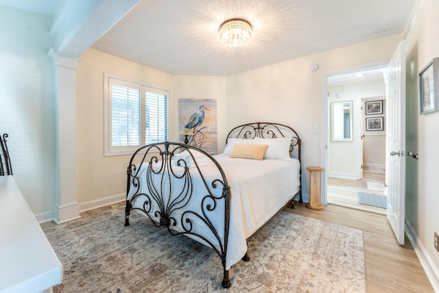 bedroom featuring decorative columns, light hardwood / wood-style floors, and a textured ceiling