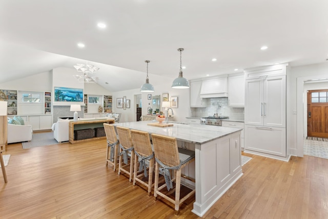 kitchen with a spacious island, a breakfast bar area, white cabinetry, pendant lighting, and light stone countertops