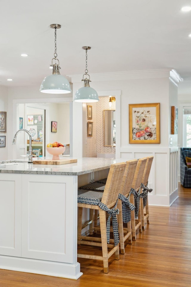 kitchen with white cabinetry, light stone counters, crown molding, decorative light fixtures, and light hardwood / wood-style floors