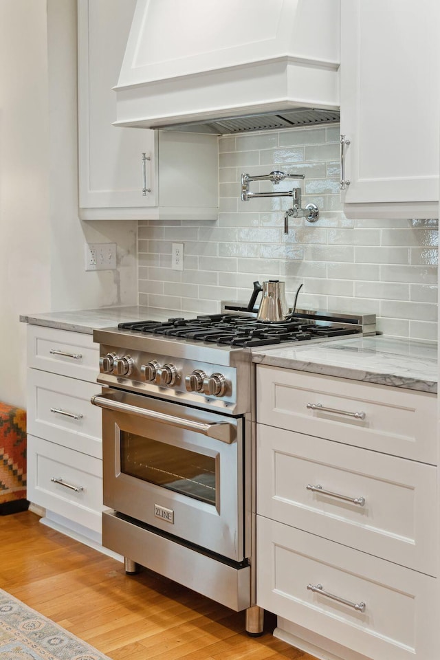 kitchen featuring custom exhaust hood, light stone counters, light hardwood / wood-style flooring, stainless steel range, and white cabinets