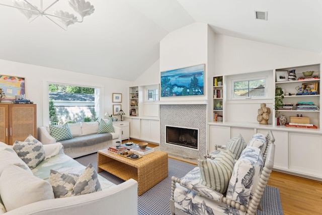 living room featuring a tile fireplace, high vaulted ceiling, light wood-type flooring, and built in shelves