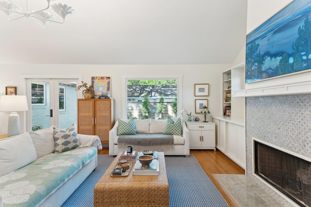 living room with a tiled fireplace, lofted ceiling, and light hardwood / wood-style floors