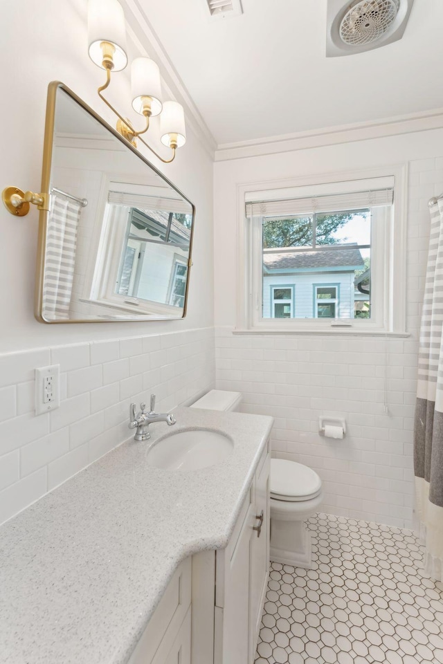 bathroom with tile patterned floors, toilet, crown molding, tile walls, and vanity