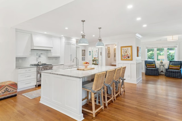 kitchen with premium range hood, white cabinets, high end stainless steel range oven, a large island, and light stone counters