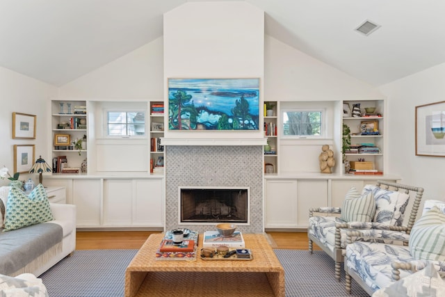 living room featuring a tiled fireplace, lofted ceiling, a wealth of natural light, and light wood-type flooring