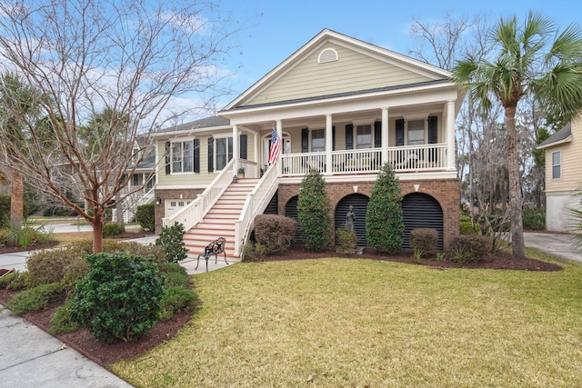 coastal inspired home with stairs, a front yard, a porch, and brick siding