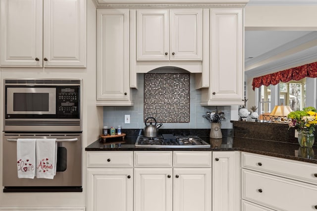 kitchen with crown molding, decorative backsplash, dark stone countertops, white cabinets, and stainless steel appliances