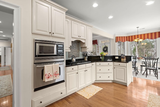 kitchen featuring a chandelier, light wood-style flooring, appliances with stainless steel finishes, and a peninsula