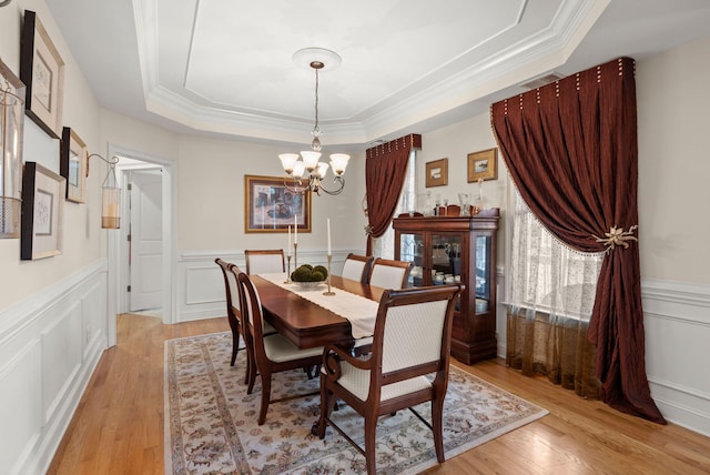 dining space featuring a wainscoted wall, a raised ceiling, a decorative wall, a notable chandelier, and light wood-type flooring