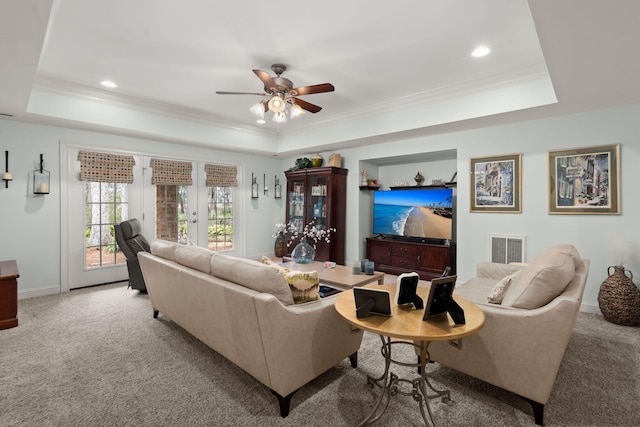 living room featuring a tray ceiling, carpet floors, visible vents, and ornamental molding