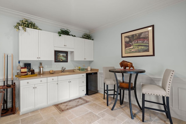 kitchen featuring white cabinetry, stone tile flooring, a sink, dishwasher, and crown molding