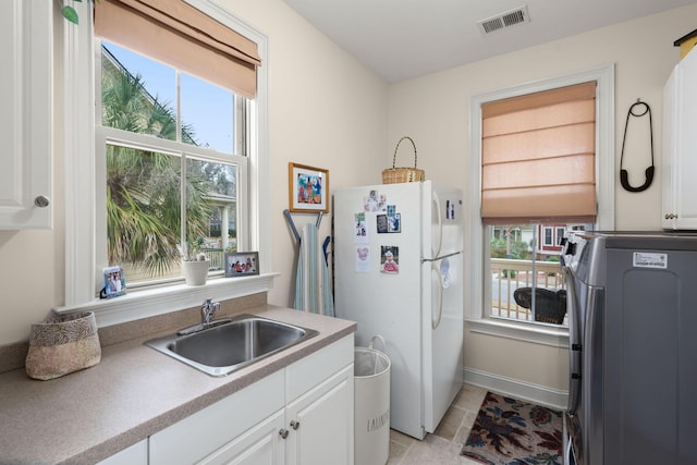 kitchen featuring a wealth of natural light, visible vents, a sink, freestanding refrigerator, and washer / dryer