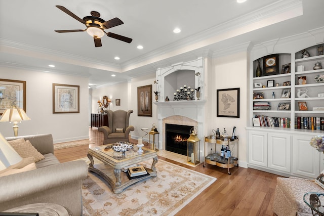 living room with light wood finished floors, a tray ceiling, recessed lighting, a high end fireplace, and ornamental molding