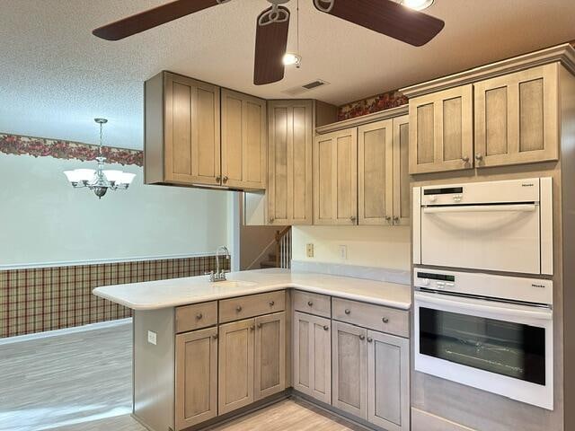 kitchen featuring white double oven, light countertops, wainscoting, a textured ceiling, and a peninsula