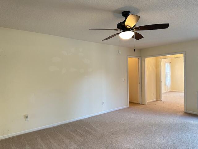 empty room with baseboards, ceiling fan, a textured ceiling, and light colored carpet