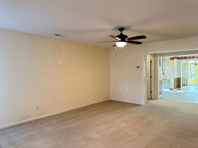 spare room featuring a ceiling fan, light colored carpet, visible vents, and baseboards