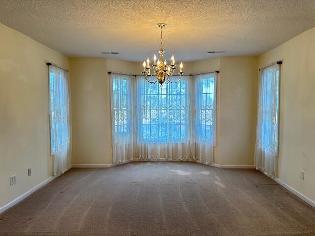 spare room featuring carpet, a textured ceiling, and a notable chandelier