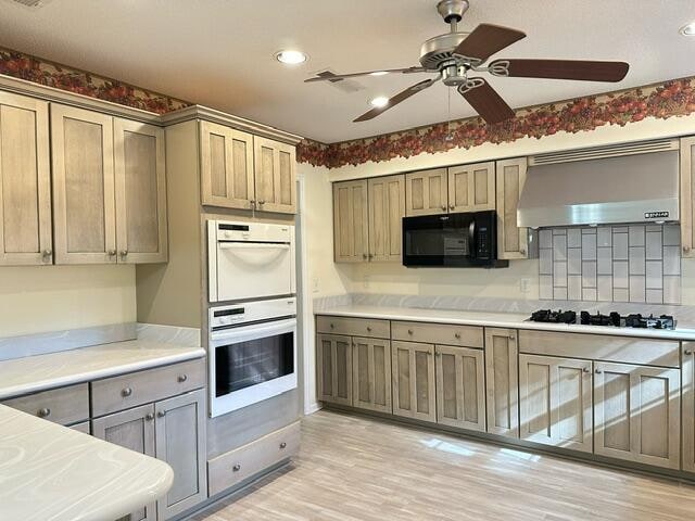 kitchen with black microwave, white double oven, gas stovetop, light countertops, and wall chimney exhaust hood