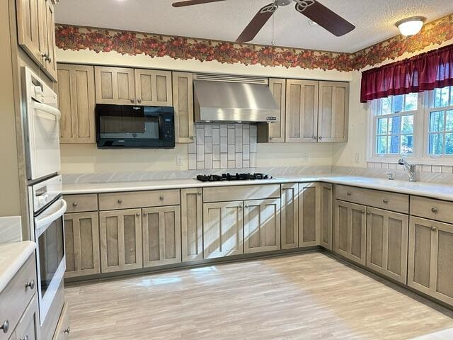 kitchen featuring gas stovetop, light wood finished floors, light countertops, black microwave, and wall chimney exhaust hood