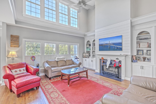 living room featuring ceiling fan, light hardwood / wood-style floors, a towering ceiling, and built in shelves