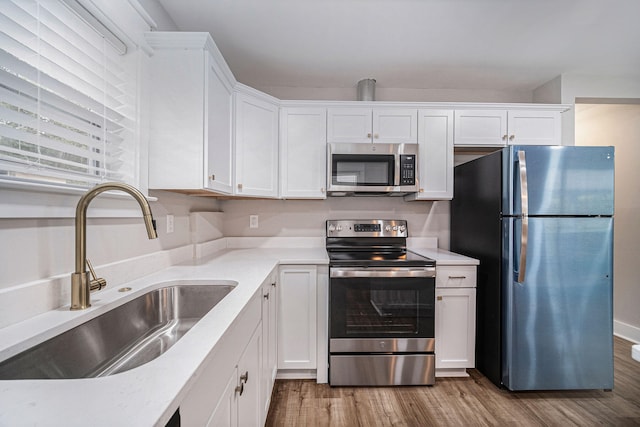 kitchen with white cabinets, appliances with stainless steel finishes, a sink, and wood finished floors