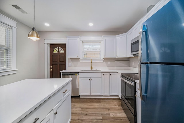 kitchen featuring appliances with stainless steel finishes, light wood-type flooring, a sink, light countertops, and white cabinetry